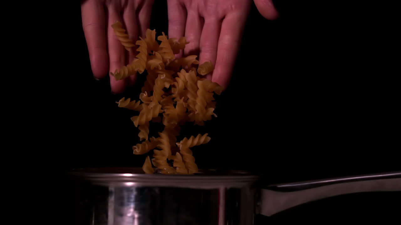 Hands dropping pasta into cooking pot
