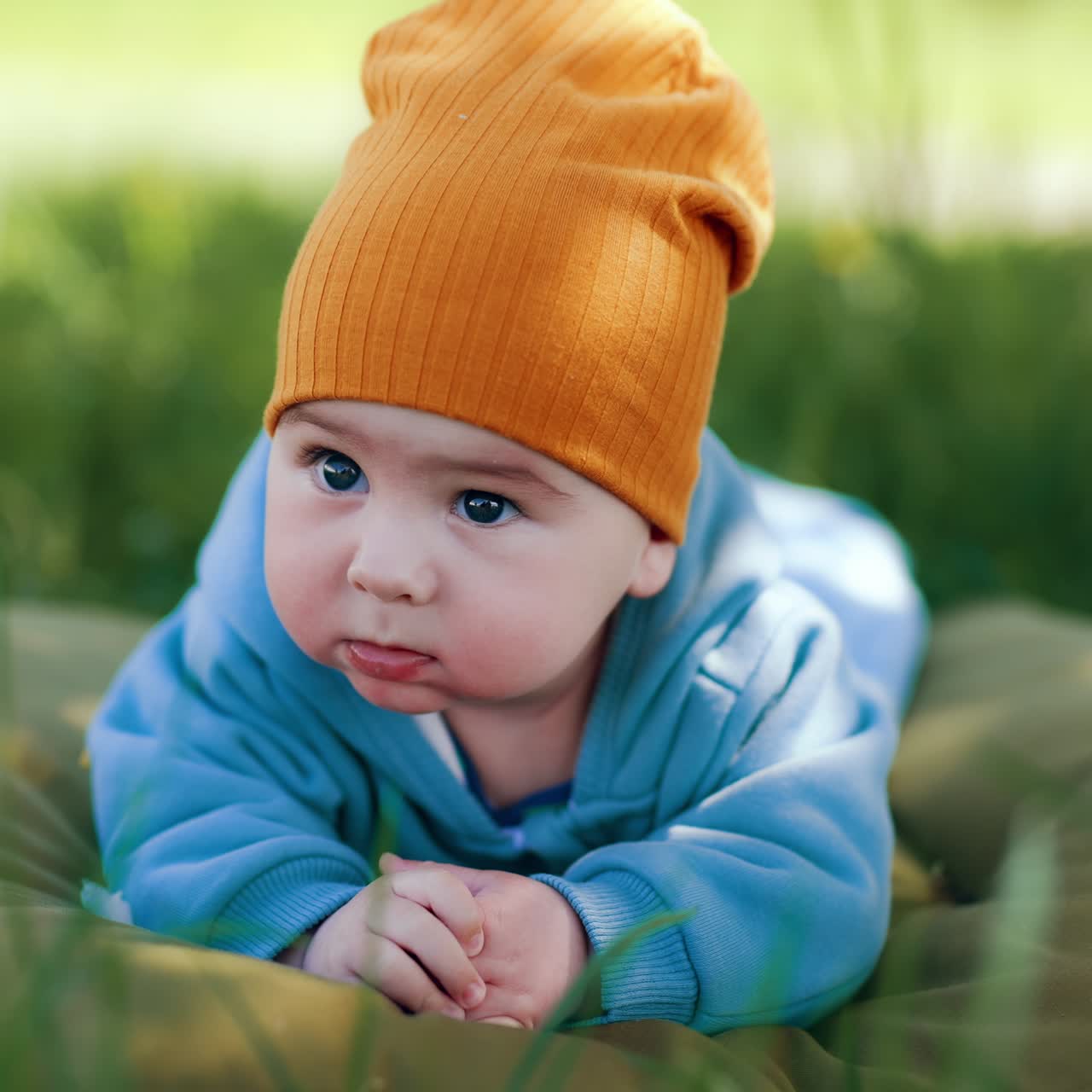 Beautiful baby boy lies on mattress outdoors with his hands folded in front of him. Cute child smiling sweetly. Close up