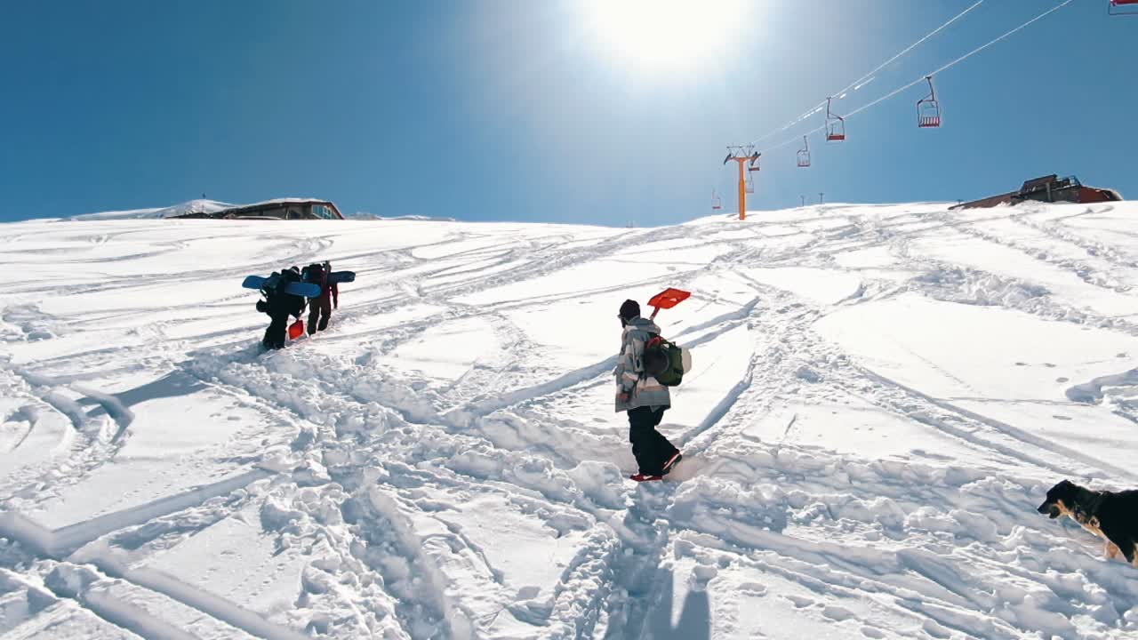 Slow motion: Snow boarders walking up the mountain. Camera moving slowly behind group of snowboarder walking up the mountain
