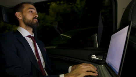 businessman in suit looking over the window of his limousine and typing on