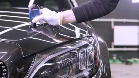 worker measures a thickness of primer on a car's body using a thickness gauge