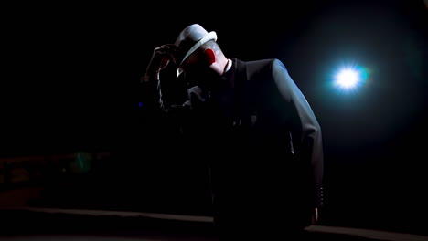 actor making a performance on theater stage. man in black suit putting on his hat and began dancing in darkness against spotlight.