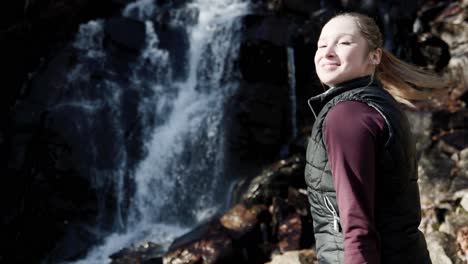 charming young caucasian girl with ponytail watching at the waterfall in a forest park at saint-come, quebec, canada