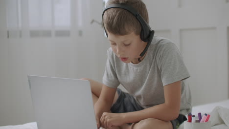 child-boy-is-staying-home-alone-drawing-on-paper-and-viewing-cartoons-by-notebook-listening-through-headphones