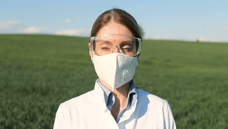 Vista-De-Cerca-De-Una-Investigadora-Caucásica-Con-Bata-Blanca-Y-Gafas-Mirando-La-Cámara-En-El-Campo-Verde