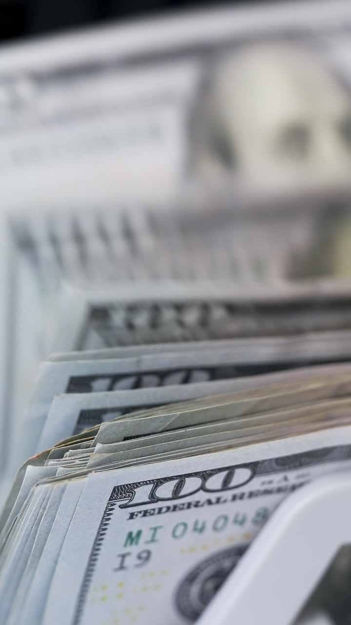 Money counting equipment for paper money calculation. Automatic mechanism for bank financial operations. Female hand taking a bundle of counted dollar bills from counting machine. Close-up. Vertical video