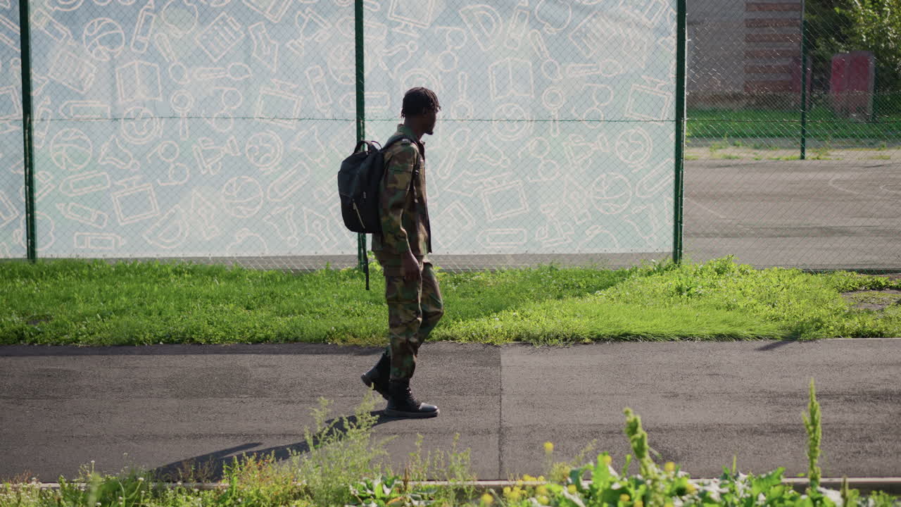 Military Scout On Sunny Path, Patrol Officer With Backpack Navigating Bright Perimeter Terrain, Military Personnel In Camouflage Taking Careful Measured Strides Beside Secured Enclosure