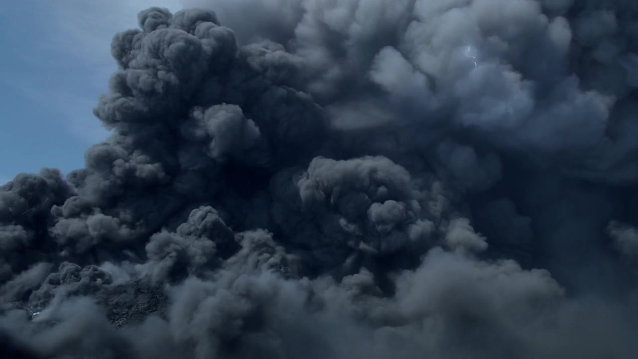 Thickening massive dark smoke plume producing forked lightning and embers against pale blue sky