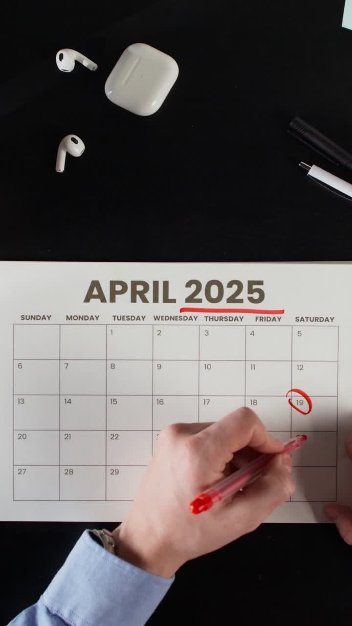 Marking a Date on April 2025 Calendar with Earbuds and Accessories