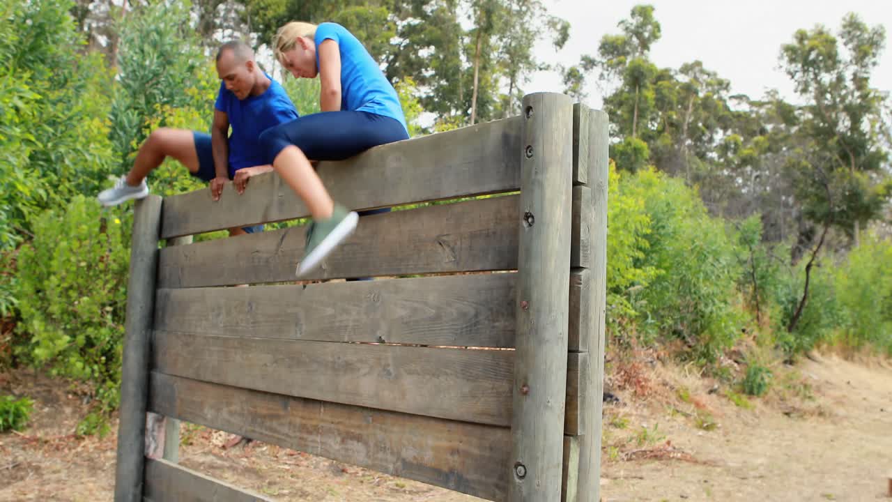 hombre y mujer aptos para escalar una pared de madera durante una carrera de obstáculos