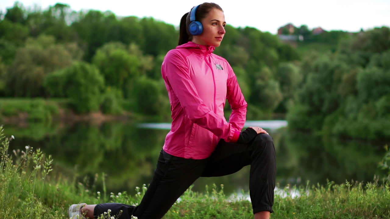 una chica con una chaqueta rosa se está preparando para una carrera de calentamiento y escuchar música en auriculares a través del teléfono