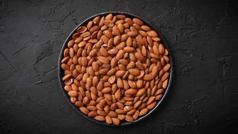nueces enteras de almendras en un plato negro colocado sobre una mesa de piedra negra