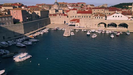 Toma-Aérea-Con-Drones-Que-Comienza-Cerca-De-Los-Barcos-En-El-Puerto-De-Dubrovnik,-Croacia-Y-Retrocede-Para-Revelar-Toda-La-Ciudad-Amurallada.