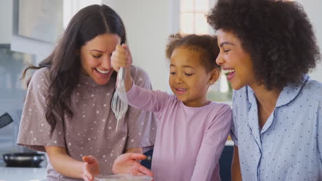 Family-With-Two-Mums-Wearing-Pyjamas-Making-Morning-Pancakes-In-Kitchen-At-Home-With-Daughter