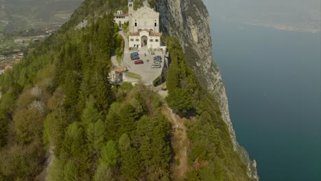 aerial overview of majestic, historic mountaintop church and rocky mountains overlooking vast waters of lake garda, italy