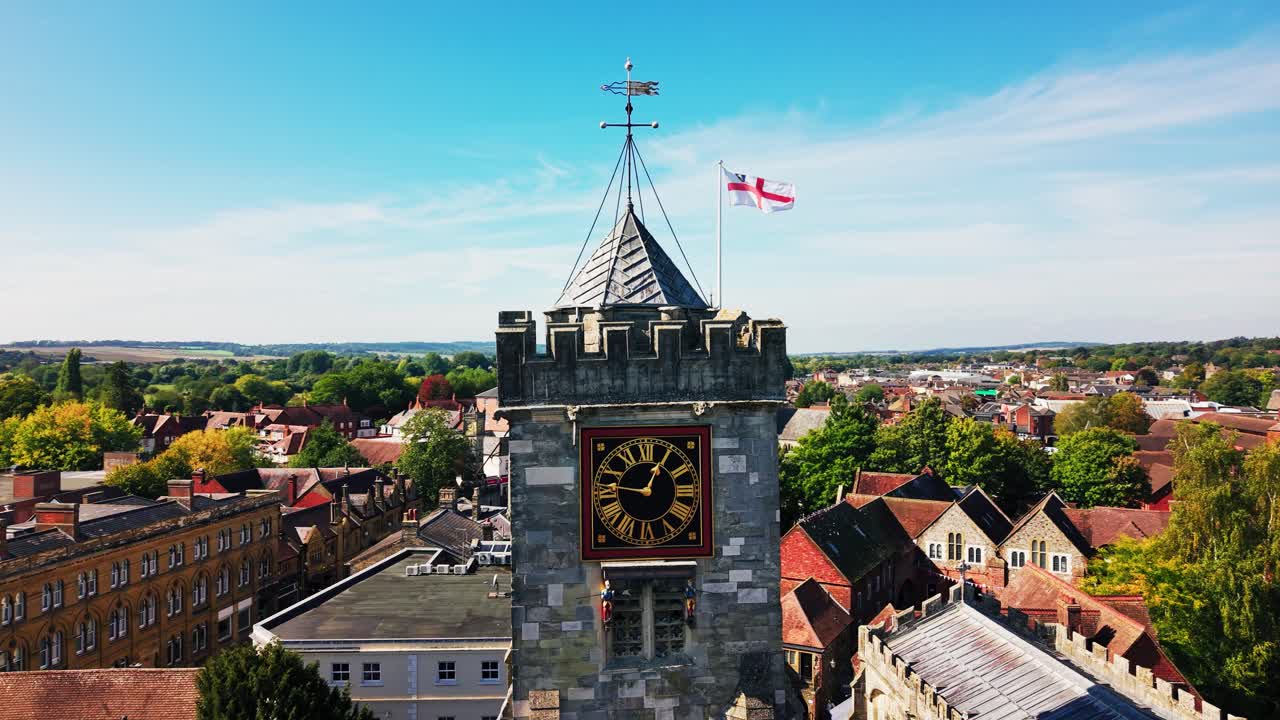 Cinematic drone aerial of the historic clock tower of St Thomas's Church in Salisbury Wiltshire England with surrounding town rooftops and countryside under blue sky