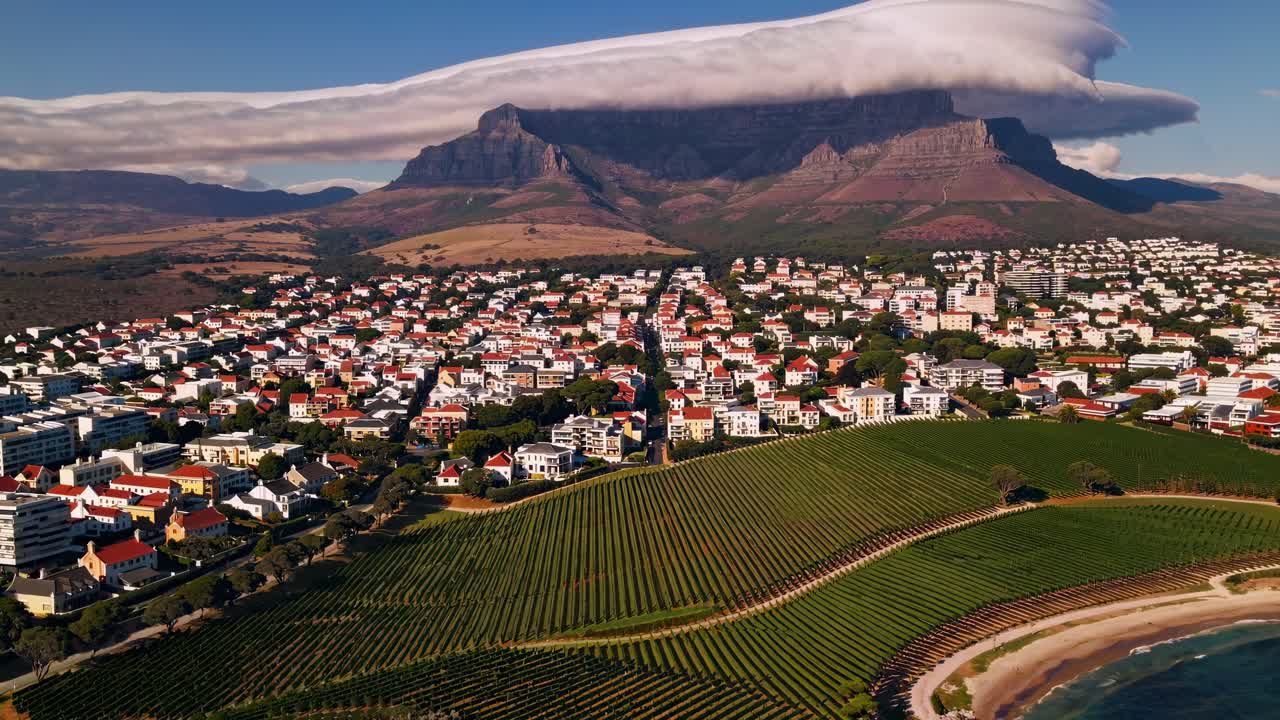Vista video aerea di una città costiera con vigneti, edifici bianchi e una montagna sormontata.