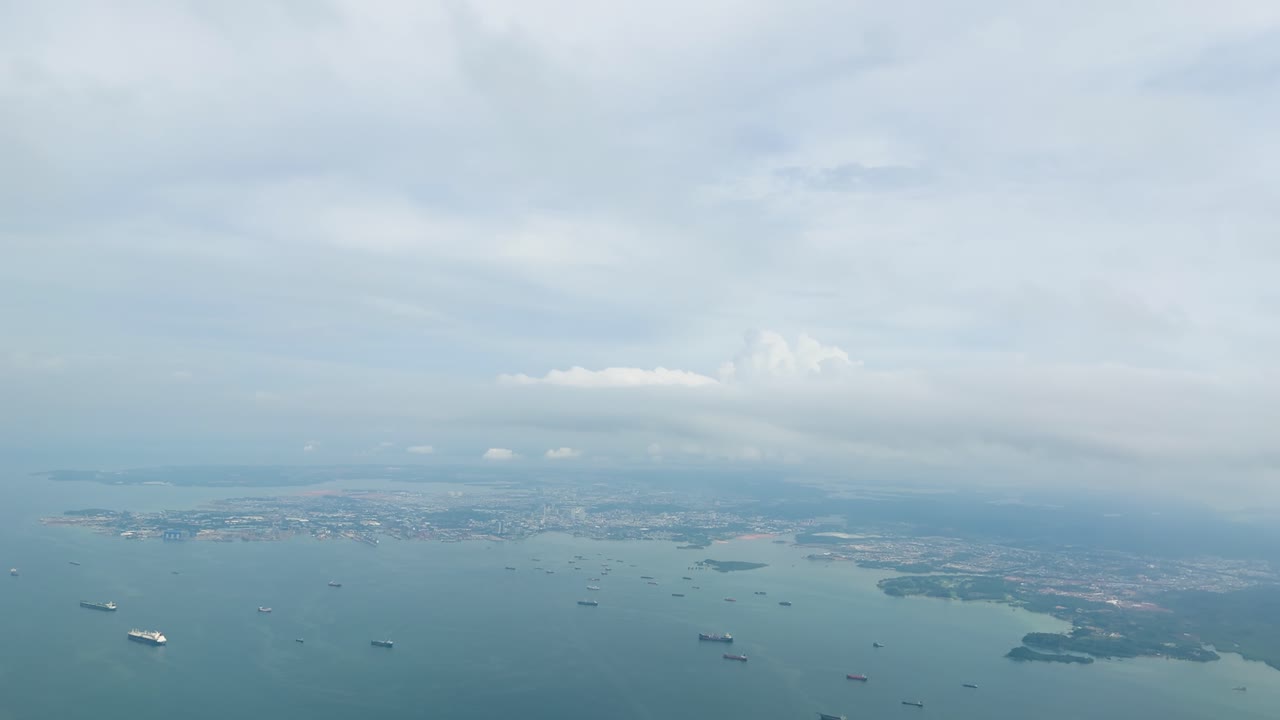 High altitude aerial shot of cargo ships approaching coastal harbor under soft overcast daylight
