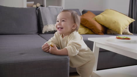 cute little girl standing next to sofa at living room and eating bread