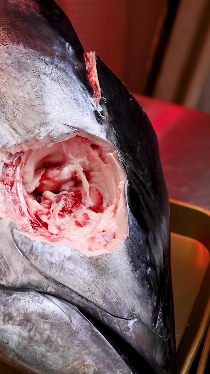 Primo piano ripreso a mano di una testa di tonno rosso cruda esposta in un mercato del pesce giapponese.