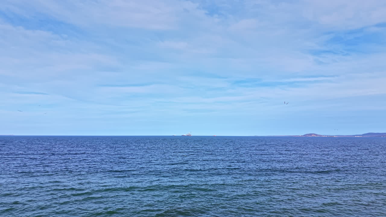 Bølger når kysten, mens både bevæger sig over horisonten under en blå himmel nær havet på en klar dag