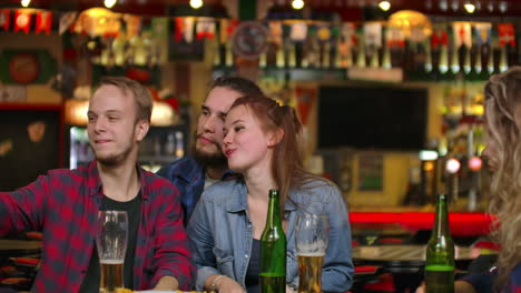 A-group-of-friends-multiethnic-resting-in-the-bar.-Friends-take-a-photo-on-the-phone-at-the-bar-make-a-shared-photo-on-the-phone.-Party-with-friends-at-the-bar-with-beer.