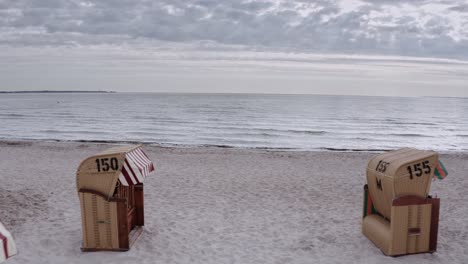 Überdachte-Korbstühle-An-Einem-Sandstrand-Mit-Blick-Auf-Das-Meer-An-Einem-Grauen,-Bewölkten-Tag-Mit-Blick-Zwischen-Den-Reihen