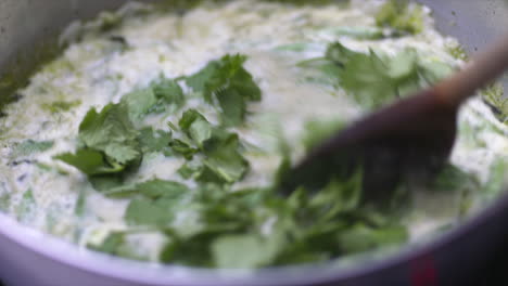 coriander being added to a saucepan of coconut milk