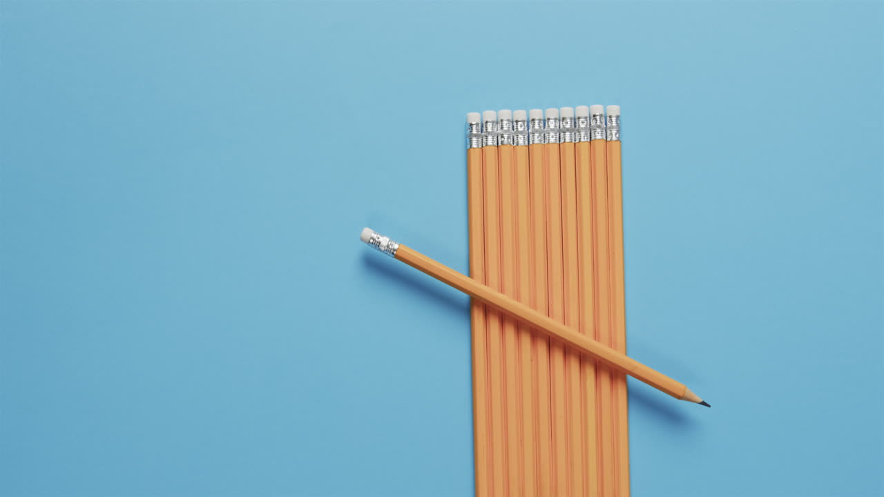 A single yellow pencil lies across a neat row of pencils on a blue background