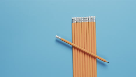 a single yellow pencil lies across a neat row of pencils on a blue background
