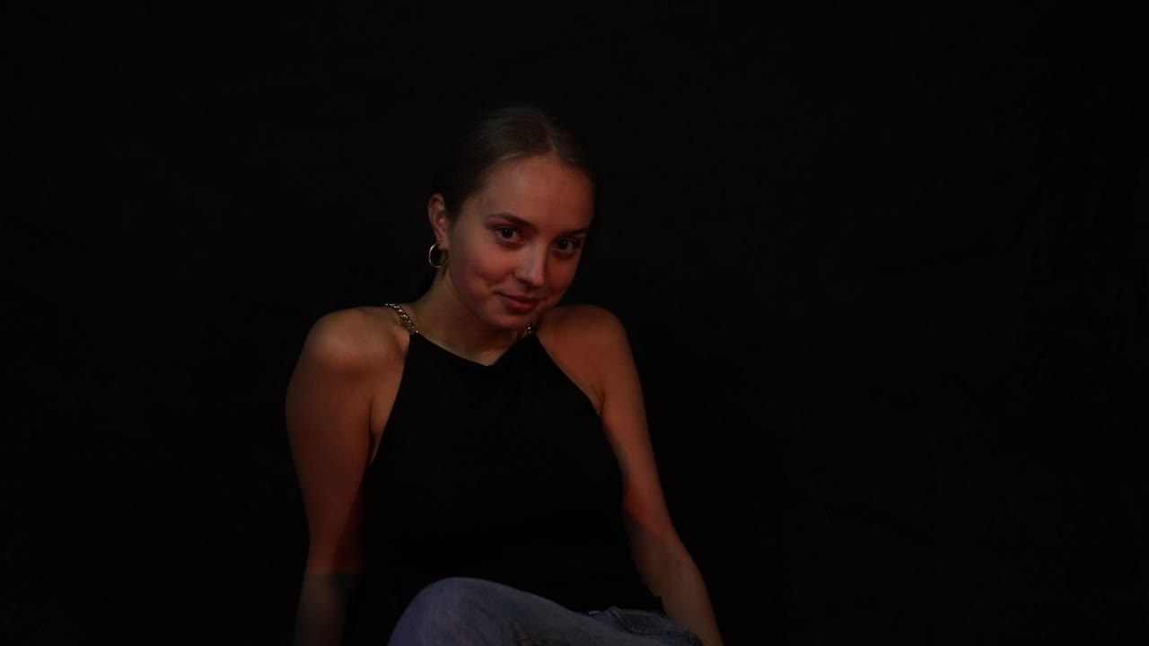 Confident teenage girl flirting while sitting in front of a black background