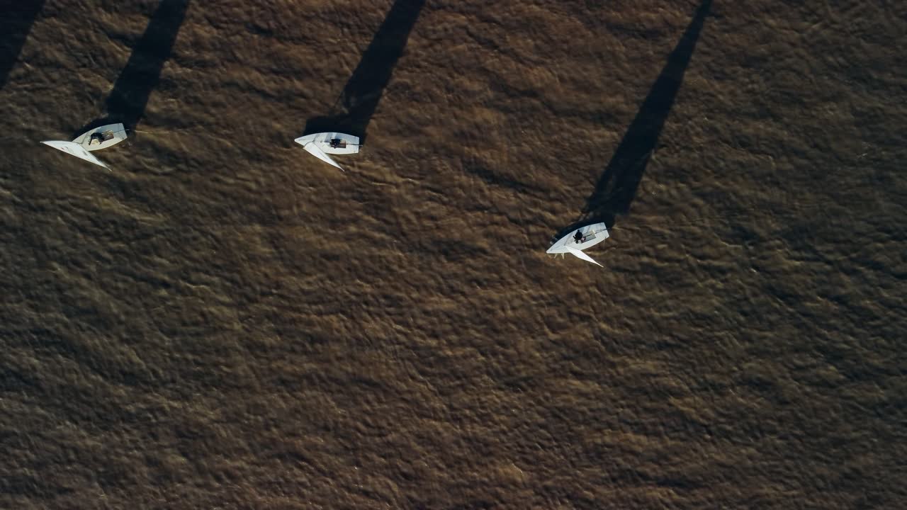 Una ripresa dall'alto con drone di piccole barche a vela che navigano da destra a sinistra. Il drone si sposta a sinistra e si allontana per rivelare altre barche