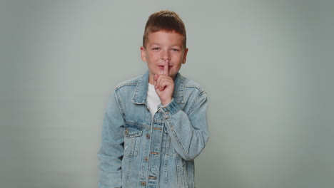 boy child presses index finger to lips makes silence gesture sign do not tells secret, shh be quiet