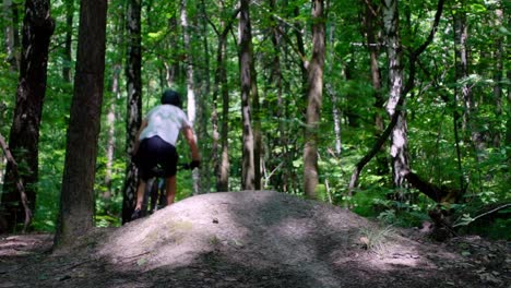 A-static-shot-in-slow-motion-of-an-adult-male-jumping-on-an-electric-bicycle-on-the-trails-in-the-forest-on-a-sunny-day-cropped-to-focus-on-the-bike