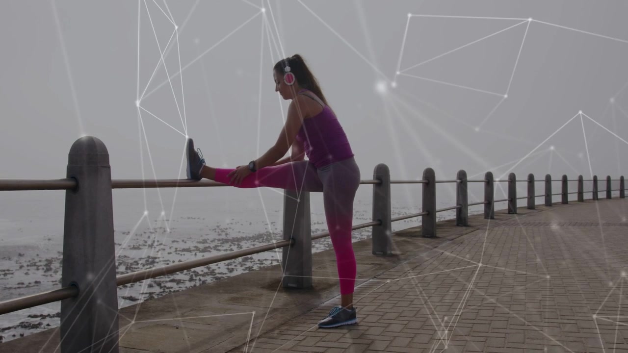 Woman placing foot on railing and stretching hamstring along coastal path, warming up for fitness