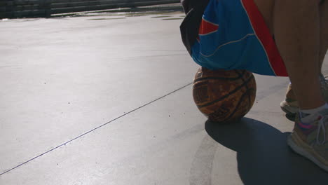 Detail-shot-of-a-young-man-on-a-basketball-on-a-street-basketball-court-with-a-sunset-sun-with-a-nice-light,-in-Barcelona,-Spain