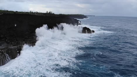 deslizándose a lo largo de una costa volcánica con acantilados de roca negra y olas rompiendo y bosque en el fondo