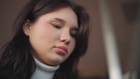 close-up of woman with pink lips, focusing on something in front of her, wearing a subtle nose ring and a golden hoop earring, soft and relaxed expression, with blurred background