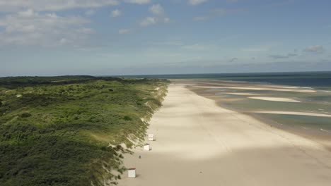 aerial shot of lush green dunes and a beautiful white beach where sand gets swept away by the wind