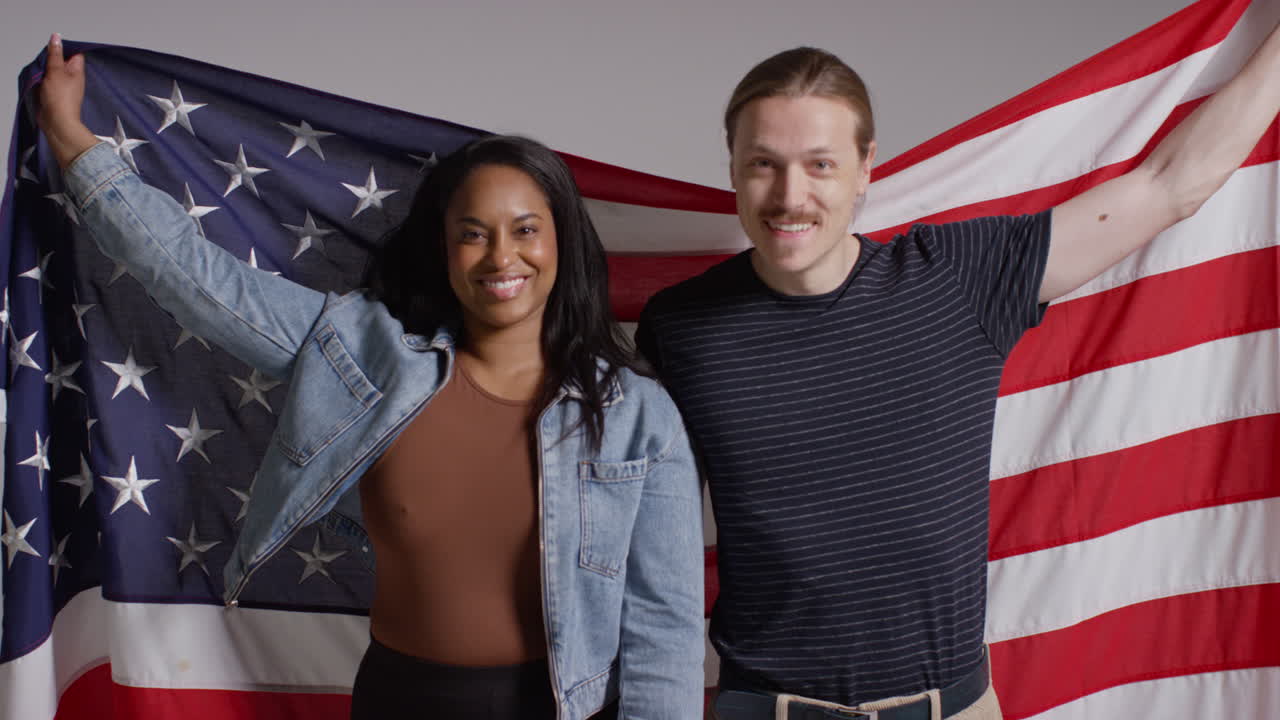 retrato de estudio de una pareja multicultural con una bandera estadounidense detrás de ellos celebrando el 4 de julio, día de la independencia 4