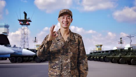 asian man soldier smiling and showing okay gesture to camera while standing at military camp