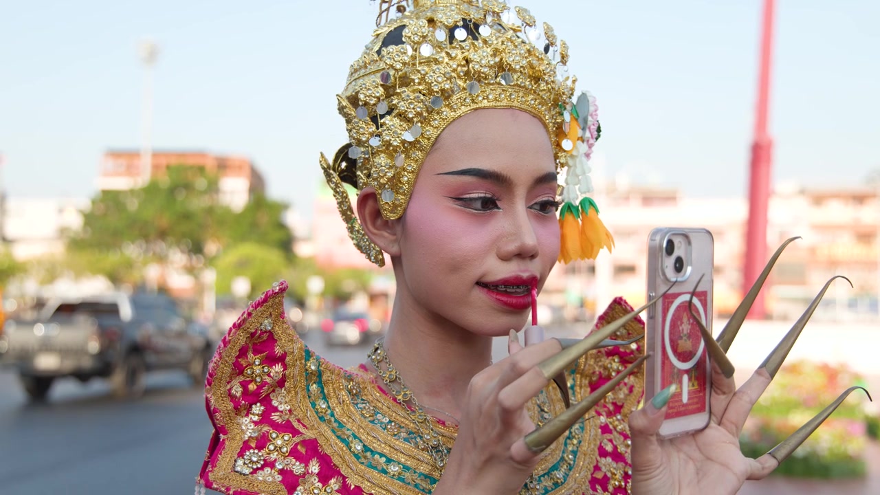 Traditionel thailandsk danser påfører læbestift, mens hun ser på sin smartphones refleksion
