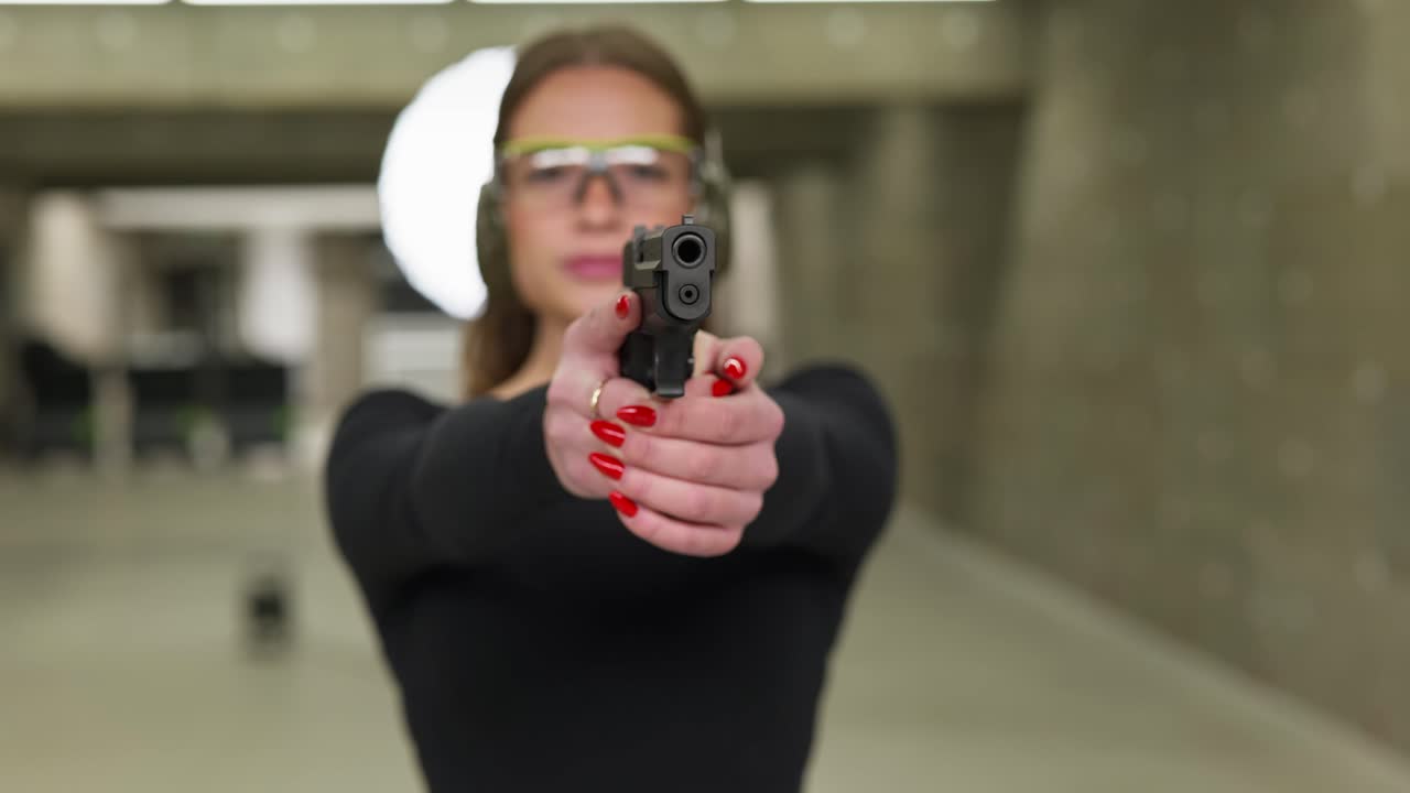 Young Woman Girl Holding a Pistol Gun with Red Nails Practicing Shooting at Range Front View Blury