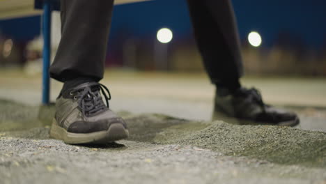 close-up of a person's feet as they repeatedly tap on the ground seated on a bench, with a blurred, dimly lit background and a building