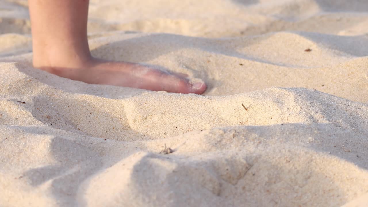 Close-up of feet gently moving and playing with sand, creating patterns and textures on a sunny beach.