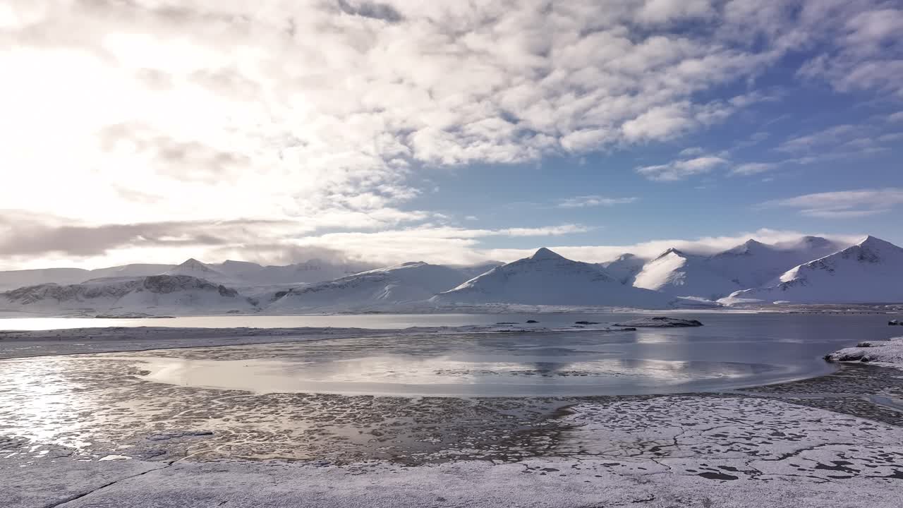 Majestic, snow-covered peaks of Hafnarfjall and Kessuhorn tower over Borgarfjörður near Borgarnes, Iceland. A tranquil winter landscape is beautifully reflected in the still fjord waters.