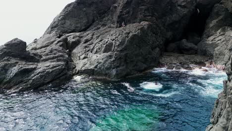Aerial pullback of cliff diver leaping into deep blue ocean waters