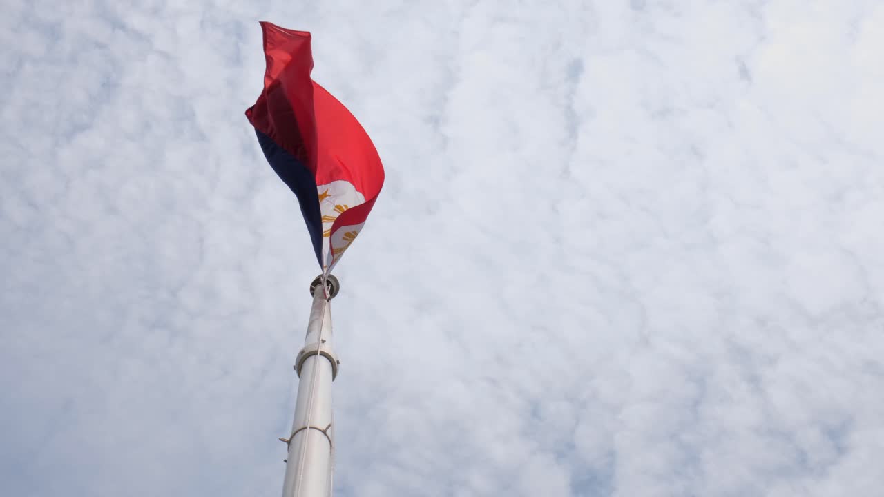 Bandiera nazionale filippina vista dal basso accanto all'asta, mentre sventola con un po' di vento e nuvole bianche simili a cotone, con la telecamera che si inclina