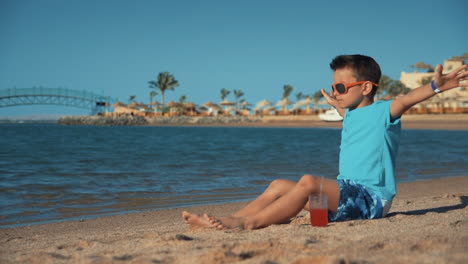 Attraktiver-Mann,-Der-Im-Sommerurlaub-Mit-Einem-Glas-Saft-An-Der-Sandküste-Sitzt.