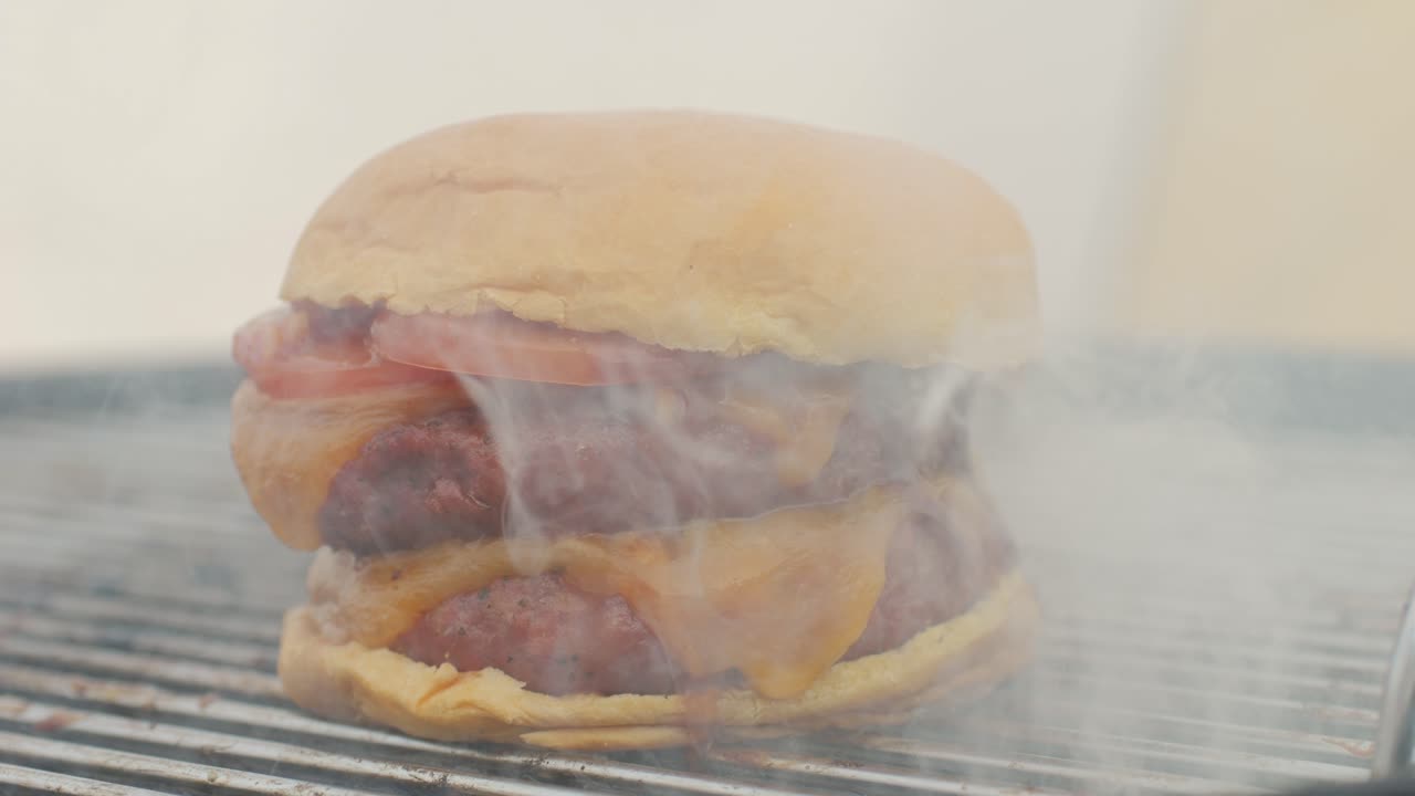 Making American fat smash burger with fresh tomatoes and cheese on grill close-up macro. Beef or pork cutlet smashing by burger press. The chef in kitchen of the restaurant making cutlets for burgers - smash burger beefsteak. Fast and street food concept.